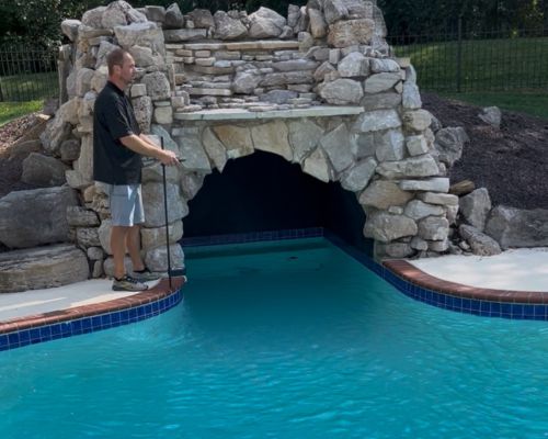 image showing an employee measuring a pool with a grotto water feature to get a new pool cover
